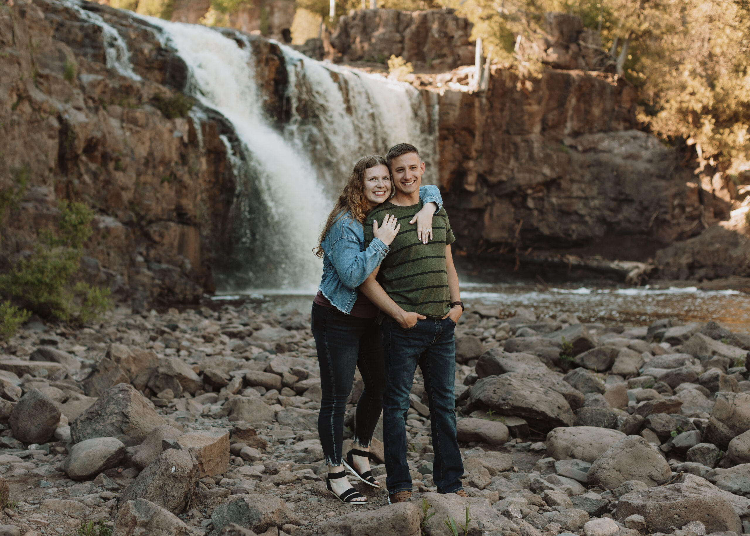 Couple embraces in front of Gooseberry Falls in Two Harbors, Minnesota during their engagement photos