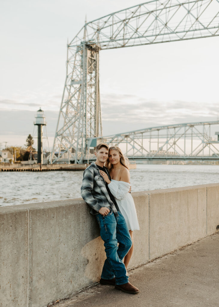 Couple embraces in front of Aerial Lift Bridge in Canal Park Duluth Minnesota during engagement photo session
