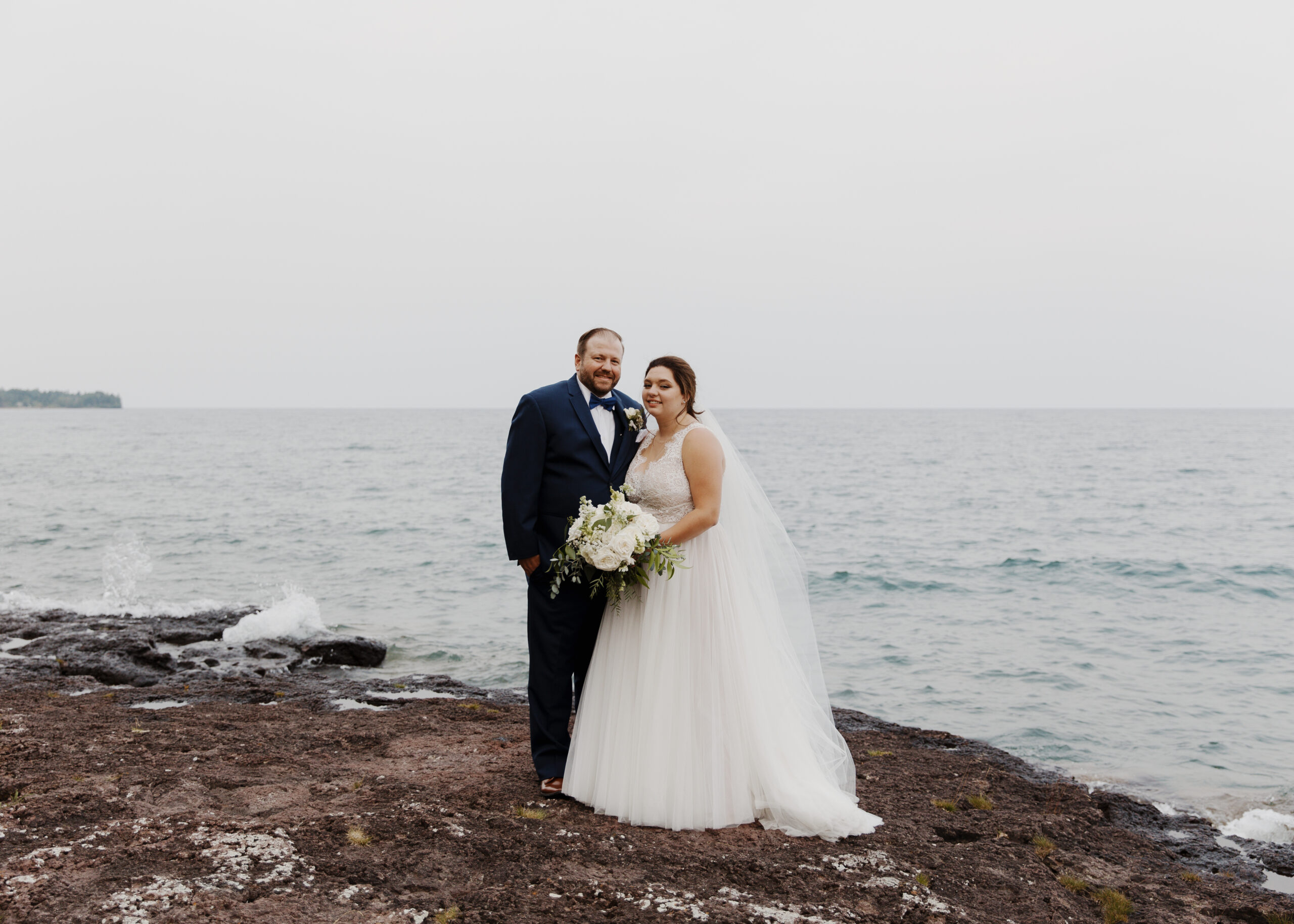 Bride and Groom pose on the shores of Lake superior during sunset in Two Harbors, Minnesota