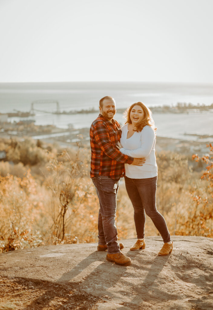 Couple poses in front of the Aerial Lift Bridge at overlook near Enger Tower during their engagement photo session in Duluth Minnesota