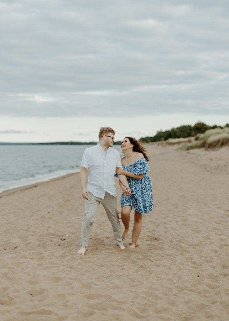 Couple walks on the beach at Park Point Beach during their Duluth Minnesota engagement photo session