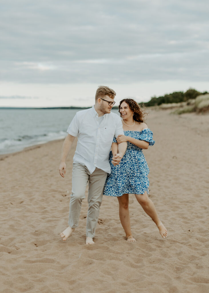 Couple walks on the beach at Park Point Beach during their Duluth Minnesota engagement photo session