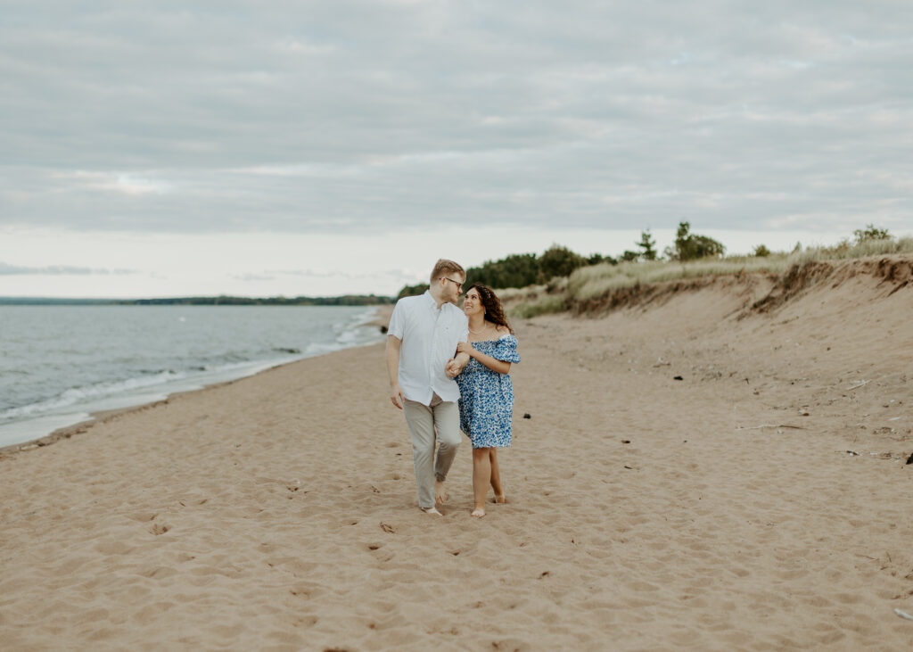 Couple walks on the beach at Park Point Beach during their Duluth Minnesota engagement photo session