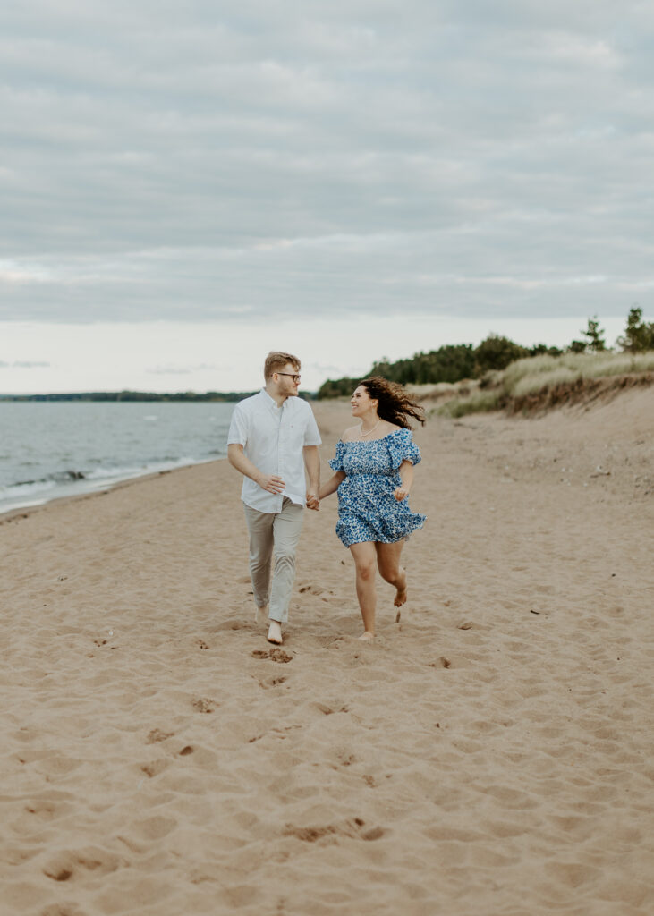 Couple runs on the beach at Park Point Beach during their Duluth Minnesota engagement photo session