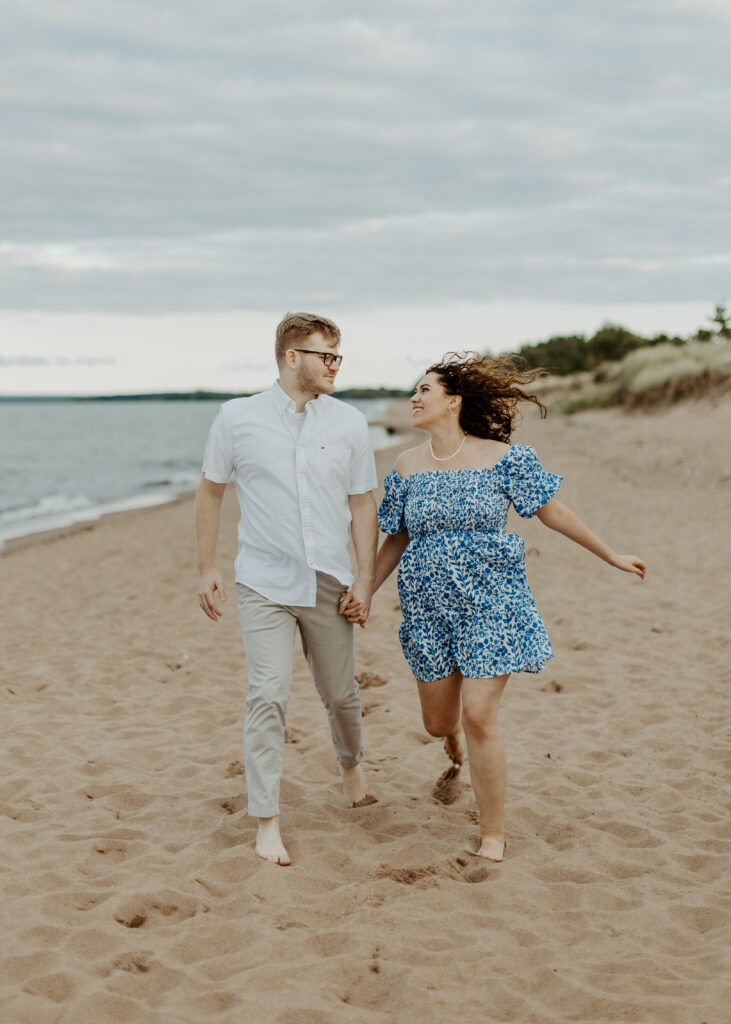 Couple runs on the beach at Park Point Beach during their Duluth Minnesota engagement photo session